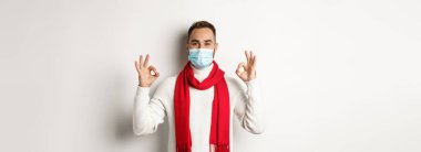 Covid-19, tecrit ve karantina konsepti. Yüz maskesi takmış tatmin olmuş yakışıklı bir adam işaret veriyor, onaylıyor ya da kabul ediyor..