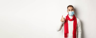Covid-19, tecrit ve karantina konsepti. Yüz maskesi takmış tatmin olmuş gülümseyen bir adam beyaz arka planda duran, başparmağını kaldıran, onaylayan ya da ürün gibi görünen.