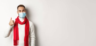 Covid-19, tecrit ve karantina konsepti. Yüz maskesi takmış tatmin olmuş gülümseyen bir adam beyaz arka planda duran, başparmağını kaldıran, onaylayan ya da ürün gibi görünen.