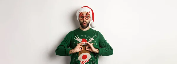 クリスマス休暇お祝いのコンセプト ハッピー男でサンタ帽子とパーティー眼鏡作る楽しいです面白いセーター 上に立って白い背景 — ストック写真