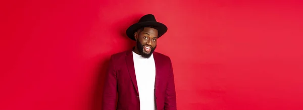 stock image Christmas shopping and people concept. Handsome bearded african american guy looking at camera, smiling confident, wearing party clothes, red background.