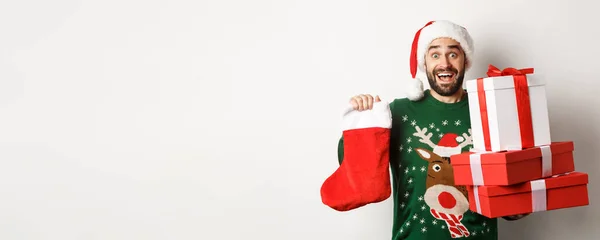 圣诞节和寒假的概念 兴奋的男人拿着圣诞袜和礼品盒 庆祝新年 把礼物放在树下 站在白色的背景上 — 图库照片
