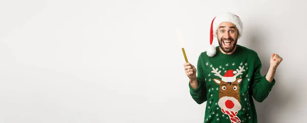圣诞派对和假期的概念 英俊的留着胡子的男人喜形于色 举行宴会 放焰火 戴着圣诞礼帽 庆祝新年 白色背景 — 图库照片