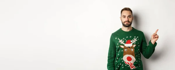 冬休みとクリスマス 右手を指差す緑色のセーターのハンサムな髭の男 プロモーションを示し 白い背景の上に立って — ストック写真