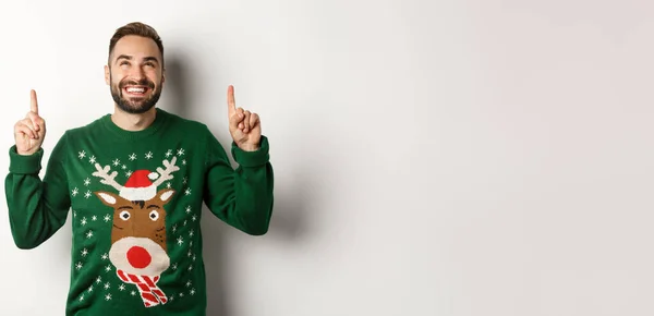 冬休みとクリスマス 白い背景の上に立って 広告を表示し 指を指して面白いセーターの幸せな笑顔の男 — ストック写真