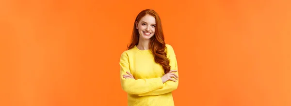人和冬天的概念 迷人的年轻女孩 红头发 黄色毛衣 站在强大而自信的姿态 笑着相机 双臂交叉在胸前 橙色背景 — 图库照片