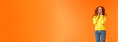 Dikey boy portre. Güzel kızıl saçlı, sıradan kot pantolonlu, sarı kazaklı, şaşırmış ve heyecanlı görün. Yüzüne yakın duran, etkilenmiş, turuncu arka planda zıplayan mutlu..