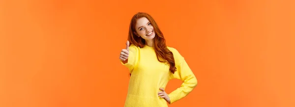 女の子の許可を与える はいと言う 黄色のセーターの陽気な赤毛の女性は腕を伸ばし 親指を見る 笑顔うなずく合意 承認を与える アイデアのように オレンジの背景喜び立って — ストック写真