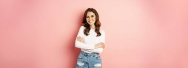 Spring and beauty. Young beautiful and stylish female model posing against pink background, cross arms on chest, smiling happy.