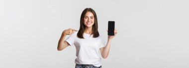 Çekici, gülümseyen bir kadın akıllı telefon ekranını işaret ediyor..
