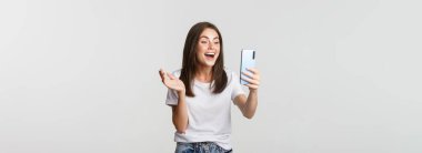 Arkadaşça gülümseyen bir kadın videosu. Akıllı telefondan arıyor ve konuşuyor. Mutlu, beyaz arka planda duruyor..