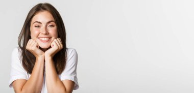 Ellerine yaslanıp hayranlıkla, beyaz bir geçmişle bakan aptal ve sevimli, gülümseyen esmer kızın yakın çekimi..