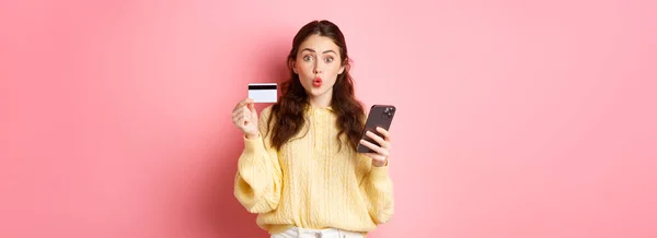 技术和网上购物 兴奋的女购物者拿着塑料信用卡 拿着手机 用智能手机付款 上网下订单 站在粉色的背景下 — 图库照片