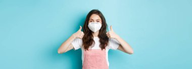 Covid, sağlık ve salgın hastalık konsepti. Solunum cihazındaki genç ve güzel bir kadının karantina süresince kişisel güvenliği düşündüğü, yüz maskesi taktığı, mavi arka plan..