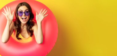 Close up portrait of enthusiastic young woman inside pink swimming ring, laughing and smiling, enjoying beach holiday, summer vacation, yellow background.