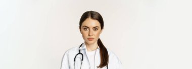 Close up portrait, face of young woman doctor with stethoscope, looking serious, professional healthcare worker in clinic, standing over white background.