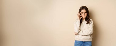 Angry woman shows mouth zipper, seal lips gesture, standing over beige background, taboo sign.