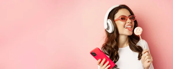 Gyönyörű Női Modell Hallgat Zenét Fejhallgató Gazdaság Lolipop Mobiltelefon Pózol — Stock Fotó