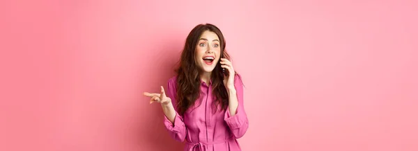 快乐的黑发女人 一边用手机聊天 一边摆出姿势 一边笑 闲聊着 站在粉色的背景上 — 图库照片