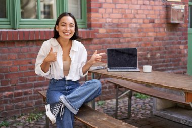 Cafe 'de dizüstü bilgisayarı, açık masası olan şık genç Asyalı kadın, reklamları işaret ediyor, afiş alanı gösteriyor..