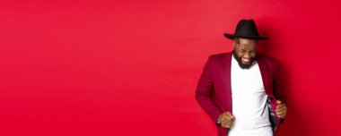 Noel ve insanlar kavramı. Mutlu siyah adam yeni yılı kutluyor ve dans ediyor, parti kıyafeti giyiyor, kırmızı arka plan.