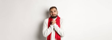 Noel tatili ve yeni yıl konsepti. Üzgün ve sefil bir adam Tanrı 'ya dua ediyor, el ele tutuşuyor, dua ediyor, gökyüzüne bakıyor ve yalvarıyor, beyaz arka planda duruyor..