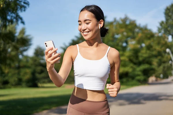 Mujer Fitness Con Botella Agua Teléfono Inteligente Trotando Parque Sonriendo — Foto de Stock