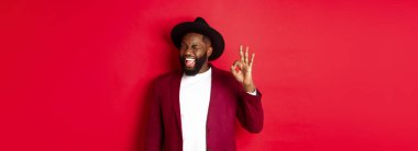 Noel alışverişi ve insanların konsepti. Yakışıklı siyah adam kendine güvenerek işaret veriyor, garanti veriyor, evet diyor, kırmızı arka planda duruyor..