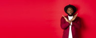 Ciddi siyahi adam görüntüsü buna şiddetle karşı çıkıyor, çapraz işaret gösteriyor, bir şeyi yasaklıyor, kırmızı arka planda duruyor..