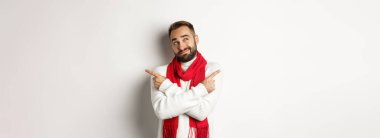 Kış tatili ve alışveriş konsepti. Adam seçim yapıyor, kararsız görünüyor, hediyelere yan bakıyor, beyaz arka planın üzerinde duruyor..