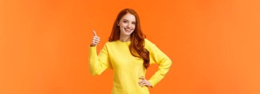 Kulağa hoş geliyor, beni de sayın. Belden yukarı vurulan neşeli neşeli kız başparmak hareketi yapar ve fikir gibi onaylayarak gülümser, tüketici için güzel bir ürün önerir, turuncu arka plan. Boşluğu kopyala