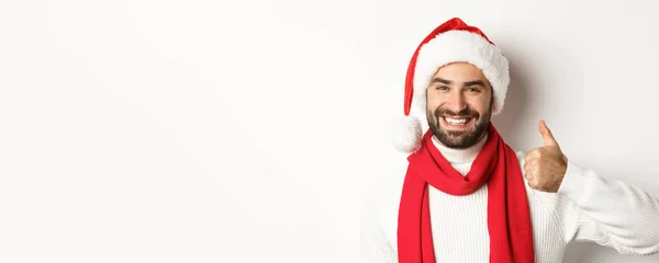 新年のパーティーや冬の休日のコンセプト サンタの帽子の幸せな男のクローズアップは 白い背景の上に立って 同意するように 承認に親指を示しています スペースのコピー — ストック写真