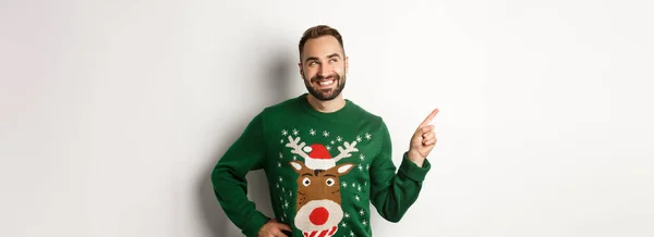 초록색 크리스마스 스웨터를 배경의 상단에 가게를 가리키며 바라보고 잘생긴 미소짓는 — 스톡 사진