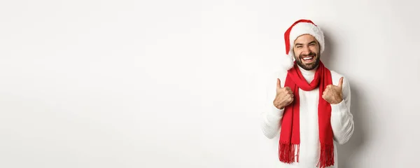 クリスマス休暇だ 新年のパーティーで幸せな男親指を見せ お祝いを楽しみ サンタの帽子と赤いスカーフ 白い背景を着て — ストック写真