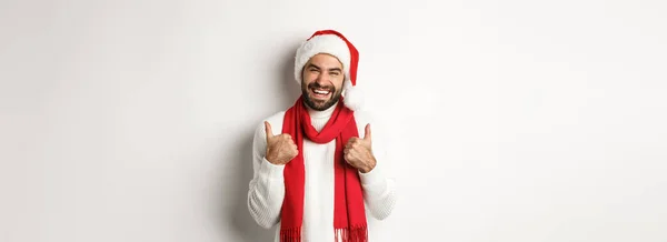 クリスマス休暇だ 新年のパーティーで幸せな男親指を見せ お祝いを楽しみ サンタの帽子と赤いスカーフ 白い背景を着て — ストック写真