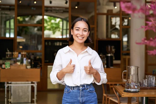 幸せなアジアの女性は親指を表示されます スミス良い好き カフェの入り口の近くに立って 彼女の勧告を与える — ストック写真