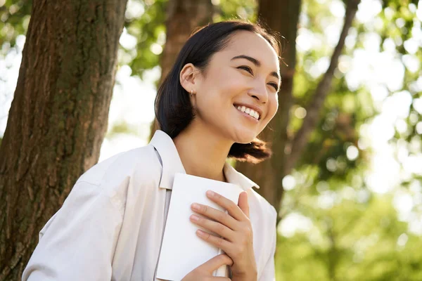 stock image Romantic smiling girl reading book in park or foret, sitting under tree shade on sunny day, relaxing on fresh air surrounded by nature.