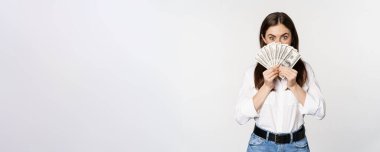Enthusiastic woman showing money, cash and smiling, got loan, micro credit, standing delighted against white background.