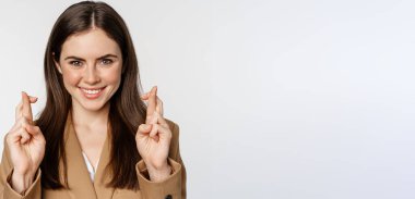 Hopeful confident businesswoman, cross fingers, smiling and making wish, praying, begging, standing over white background.