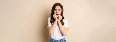 Portrait of scared woman trembling, watching smth scary and looking insecure timid, posing against beige background.