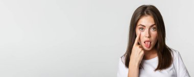 Dilini gösteren, göz kapağını çeken, seni izleyen aptal, çekici genç kızın yakın çekimi..