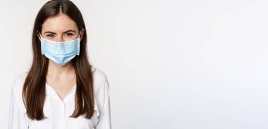 Covid-19 and pandemic concept. Young office woman wearing medical mask during coronavirus social distancing, standing over white background.