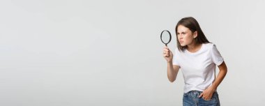 Ciddi görünümlü çekici bir genç kadın bir şey arıyor, büyüteçten bakıyor, beyaz arka plan..