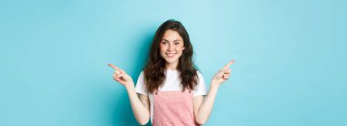Parlak makyajlı güzel bir kız imajı, parmaklarını yana çevirip gülümsüyor, iki çeşit promosyon teklifi sunuyor, seçenekler sunuyor, mavi arka plan..
