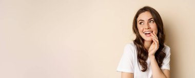 Close up portrait of coquettish beautiful girl gazing silly, gently smiling and giggling, posing flirty and cute against beige background. Women beauty and valentines concept.