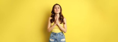 Desperate sad woman asking for help, begging with pray, need something, supplicating or praying, standing over yellow background. copy space