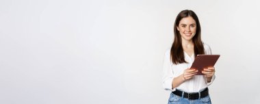 Portrait of smiling corporate woman looking at digital tablet, working, standing over white background.