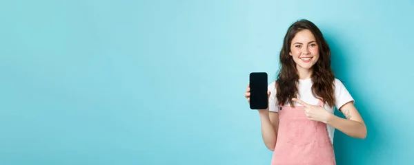 Szczęśliwa Uśmiechnięta Brunetka Wskazująca Palcem Pusty Ekran Smartfona Polecająca Sklep — Zdjęcie stockowe