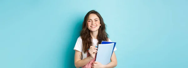 青を背景に春の服に身を包み コースノートを持ってカメラで微笑む幸せな若い女子学生 — ストック写真
