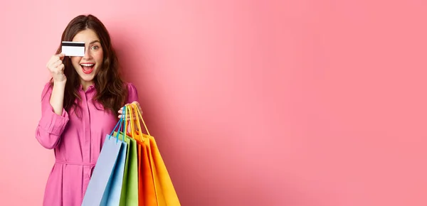 兴奋而快乐的女人拿着购物袋 拿着塑料信用卡 面带微笑 站在粉色背景下的画像 — 图库照片
